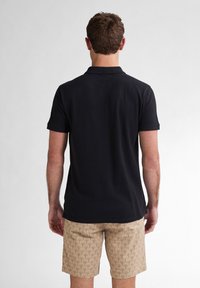 Polo shirt navy a maniche corte, tessuto testurizzato e vestibilità standard, abbinato a pantaloni corti beige con un motivo a foglie di palma.