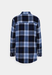 Chemise en flanelle à carreaux bleu et noir, manches longues, poignets boutonnés, présentant un mélange de carrés clairs et foncés avec des accents gris.