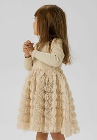 Hellbeige Kleid mit einem taillierten Langarm-Oberteil und einem gestuften Rock, der aus Stoffrosetten besteht. Weiche Textur, geraffte Taillendetails.