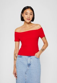 Top aderente rosso a spalle scoperte realizzato in tessuto a costine, maniche corte, abbinato a una gonna di jeans azzurri chiari con tasche e cucitura verticale.