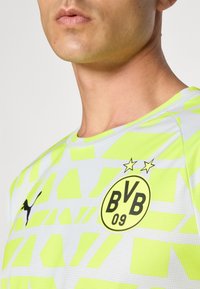 Camiseta deportiva amarilla y gris con patrones geométricos, logo redondo con "BVB 09" en el frente y la marca Puma en negro en el costado.