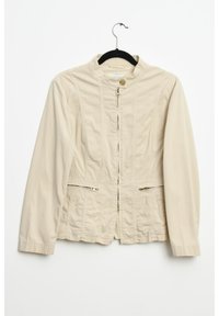 Beige sako s vysokým límcem, předním zipem a dvěma kapsami na zip. Vyrobeno z hladké tkaniny, se subtilními švy.