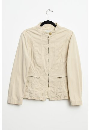 Veste beige avec un col montant, fermeture éclair à l'avant et deux poches zippées. Fabriquée en tissu lisse, elle présente des détails de couture subtils.