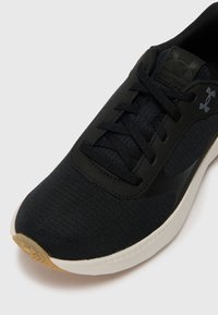 Chaussure de sport noire en mesh et matières synthétiques, avec des lacets plats, une tige texturée et une semelle en caoutchouc de couleur claire.