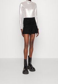 Metallisch silbernes Langarmshirt, kombiniert mit einem schwarzen gerafften Minirock mit Kordelzug, getragen mit klobigen schwarzen Stiefeletten.