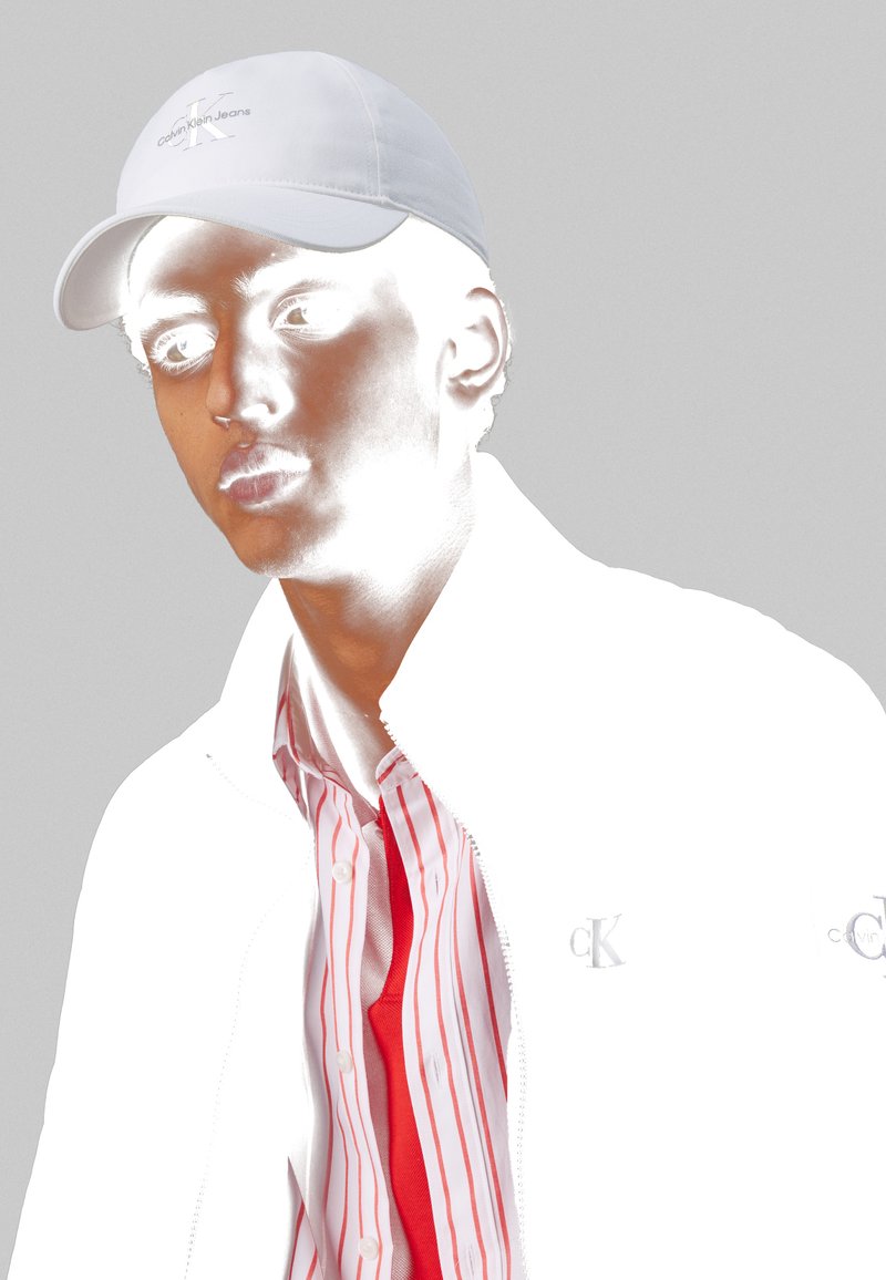 Casquette blanche avec le logo "Calvin Klein Jeans", veste blanche et chemise rouge à rayures verticales ; couleurs à fort contraste ; texture lisse.