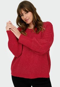 Maglione rosso a maglia con polsini larghi e vestibilità rilassata. Presenta un motivo tessurizzato e un collo rotondo, abbinato a pantaloni neri.