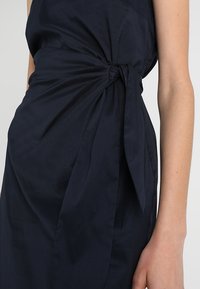 Granatowa sukienka z gładkiego materiału, z węzłem w talii i zwiewnym krojem z jednej strony.