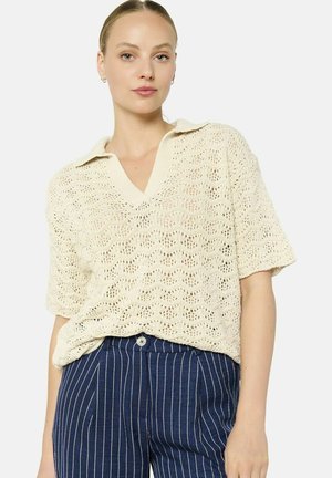 Beige knitted polo shirt with a loose fit, featuring a V-neck and short sleeves. The texture shows an open weave pattern.