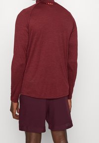 Bordeaux långärmad träningströja med hög krage och en diskret textur, i kombination med matchande shorts med en liten perforerad detalj.