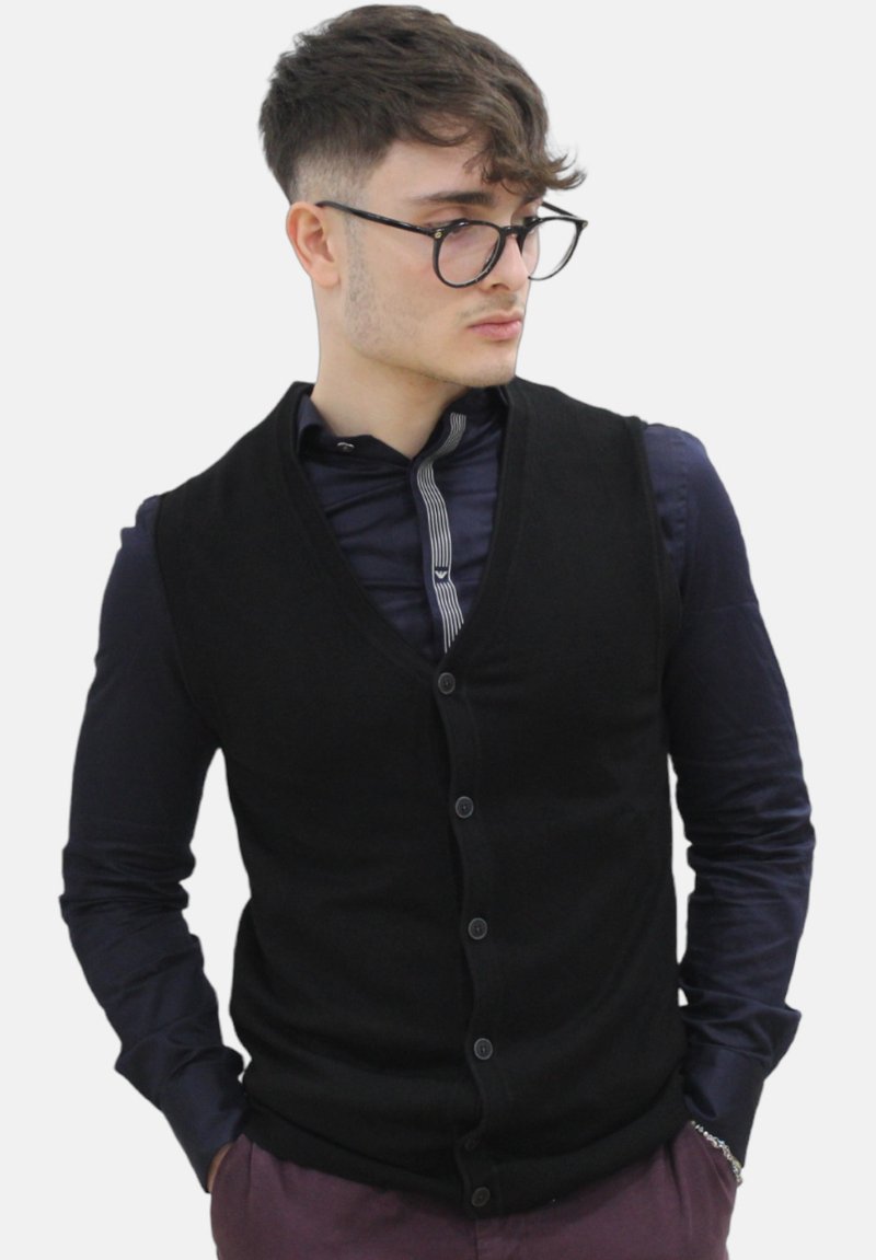 Zwarte gebreide vest met een V-hals ontwerp, voorzien van een knoopsluiting aan de voorkant, gedragen over een marineblauw shirt met een gestreepte kraag.