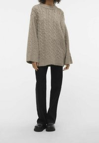 Beige knitted sweater with a cable pattern, round neckline, and wide sleeves, paired with black flared pants and chunky black shoes.