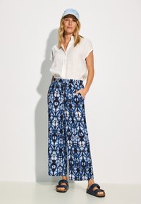 White short-sleeve button-up shirt, blue patterned wide-leg pants, and navy sandals. The pants feature a geometric design in blue shades.