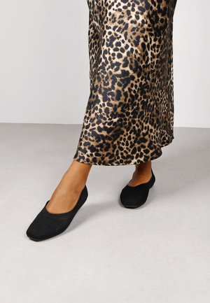 Ballerine nere in rete con un motivo testurizzato, abbinate a una gonna leopardata con tonalità di marrone e nero. Design con suola piatta.