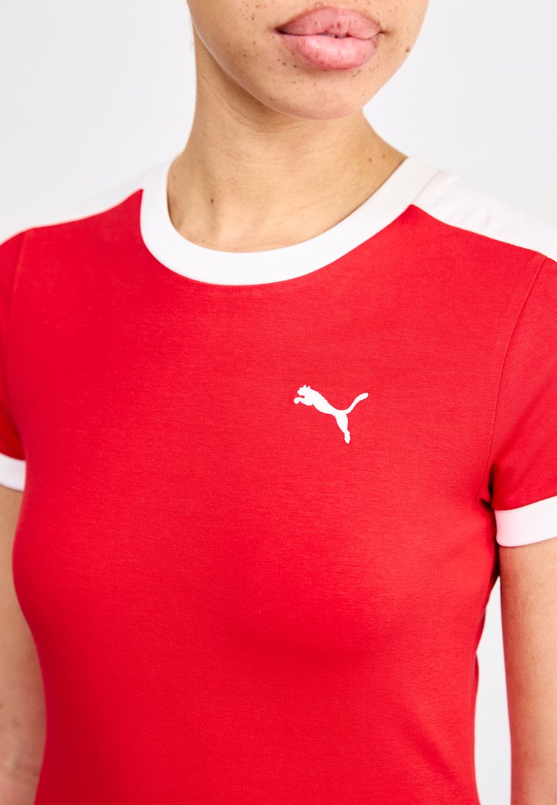 Camisa roja de manga corta hecha de tela suave, con un cuello redondo blanco y detalles blancos en las mangas, además de un pequeño logo blanco.