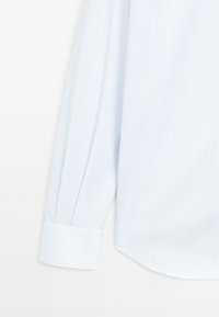 Camicia a strisce blu chiaro con maniche lunghe, realizzata in tessuto morbido. Presenta un polsino con bottone e un orlo curvato per un aspetto sartoriale.