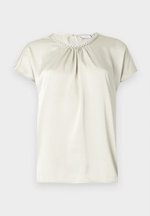 Blouse à manches courtes en satin beige clair avec un col froncé orné de petites perles nacrées et une fermeture discrète au dos.