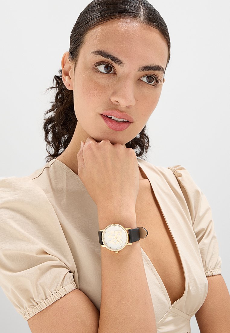 Gold-weißes Armbanduhr mit rundem Zifferblatt und schwarzischem Armband. Das Zifferblatt hat ein minimalistisches Design und ist am Rand mit Kristallen akzentuiert.