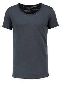 T-shirt à manches courtes et col rond en gris foncé. Tissu doux et lisse avec une empiecement arrière légèrement plus long. Étiquettes visibles à l'intérieur de l'encolure.