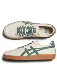 Paire de baskets basses crème et vertes avec bout perforé, semelle en gomme et bandes latérales vertes croisées, vues de dessus et de côté.