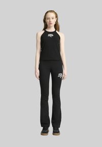 Top senza maniche nero e pantaloni neri a palazzo con un design aderente. Presenta un logo Puma bianco sia sul top che sui pantaloni.