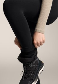 Leggings noirs portés avec un haut beige côtelé, mis en valeur par une botte noire avec des lacets gris et un revers texturé. Matériaux lisses et design ajusté.