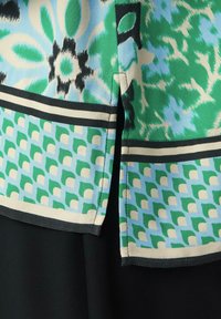 Multicoloroberteil mit floralen und geometrischen Mustern in Blau-, Grün- und Schwarztönen sowie kontrastierenden Rändern. Glatter Stoff.