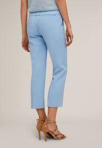Pantalons ajustés bleu clair avec une coupe cropped et des poches latérales, associés à des sandales à talons hauts beiges avec des lanières délicates.