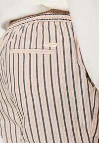 Pantaloni in tessuto a righe di colore rosa chiaro e blu navy, con vita elastica arricciata e una tasca applicata; etichetta del marchio visibile.