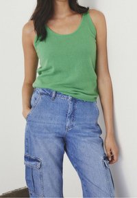 Top sin mangas verde de tejido suave combinado con pantalones cargo de mezclilla azules que cuentan con bolsillos laterales y un ajuste relajado.