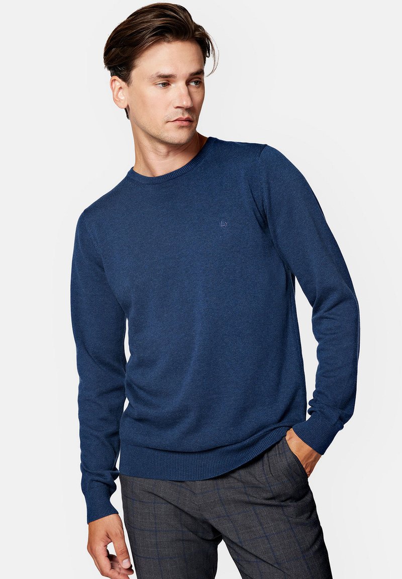 Navy niebieski sweter z okrągłym dekoltem, wykonany z miękkiej dzianiny, z prążkowanymi mankietami i dołem. Posiada subtelne logo na piersi. Zestawiony z wzorzystymi spodniami.