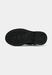 Suola nera di scarpa con motivi del battistrada a forma di cuore e dettagli del marchio su uno sfondo bianco piatto.
