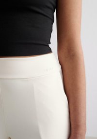 Hooggewaist crèmekleurige sportleggings met een gladde afwerking en subtiele branding op de tailleband, gecombineerd met een aansluitend zwart topje.