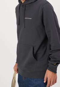 Felpa con cappuccio grigia scura in morbido tessuto, con tasca frontale e cappuccio regolabile. Logo ricamato "Lyle & Scott" sul petto, con un piccolo accento del logo sulla manica.