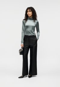 Ελαφρύ τιρκουάζ μπλουζάκι με μακριά μανίκια και ψηλό λαιμό, συνδυασμένο με μαύρο παντελόνι φαρδιάς γραμμής. Μαύρα μυτερά παπούτσια και μια μικρή μαύρη τσάντα ολοκληρώνουν την εμφάνιση.