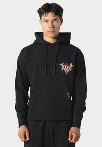 Felpa nera con cappuccio realizzata in cotone, con lacci, tasca frontale e logo triangolare ricamato con dettagli floreali sul petto.