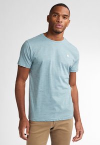 Light blue short-sleeve t-shirt with a crew neck, textured fabric featuring subtle patterns, and a small logo patch on the chest.