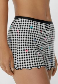 Zwart-witte geruite shorts met meerkleurige hartpatronen. Heeft een golvende zoom en een zwarte elastische tailleband.