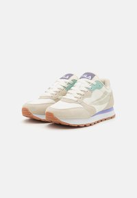Zapatillas en beige y verde menta con material de ante y malla, con cordones blancos, acentos morados y una suela de goma marrón claro.