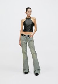 Μαύρο δερμάτινο τοπ με στρογγυλή λαιμόκοψη, γκρι τζιν με φαρδύ καμπάνα και ξεθωριασμένη υφή, μαύρη ζώνη με μεταλλική αγκράφα, μαύρα μπότες με τακούνι.