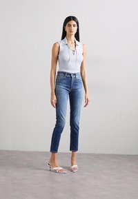 Top sin mangas de rayas azul claro con cuello, combinado con jeans ajustados de lavado medio y tacones de tiras blancos, sobre un fondo liso.