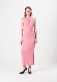 Pink, sleeveless maxi dress with gathered detailing at the front and side slit. Model wearing black high-heeled shoes. Smooth, stretchy fabric.