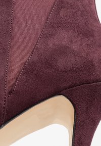 Tacchi alti in suede bordeaux con una superficie liscia, pannello in tessuto texture e design a punta, caratterizzati da un accento in plastica trasparente sul tacco.