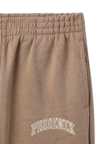 Pantaloni tuta marroni con cintura elastica, tasche laterali e "PHOENIX" ricamato in bianco. Il tessuto appare morbido e testurizzato.