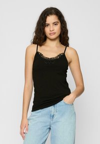 Svart tanktopp med blonderende kant ved utringningen, med tynne justerbare stropper. Kombinert med lyseblå denim bukser med høy livlinje.
