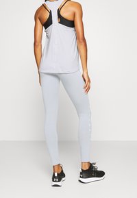 Completo sportivo composto da una canotta grigia chiaro con dettagli neri e schiena a chiave, abbinata a leggings grigi chiaro aderenti e sneakers nere.
