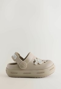 Sabot beige à enfiler en caoutchouc, avec des trous de ventilation, un logo en relief et une bride de talon ajustable. Semelle texturée pour une meilleure adhérence.