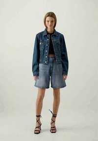 Takkihousu tummansinisenä napituksessa ja taskuilla, käytössä mustan crop-topin päällä. Yhdistetty vaaleansinisiin farkkushortseihin ja mustiin remmisandaaleihin.