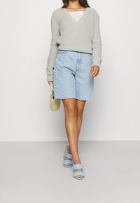 Jasnoszary, dziany sweter z dekoltem w serek, zestawiony z jasnoniebieskimi szortami dżinsowymi z postrzępionymi brzegami. Niebieskie plecione klapki i pleciona torba.