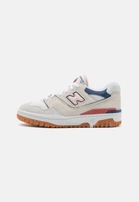 Sneaker with a cream suede upper, navy accents, and red detailing. Features a white midsole and gum rubber outsole with a textured pattern.